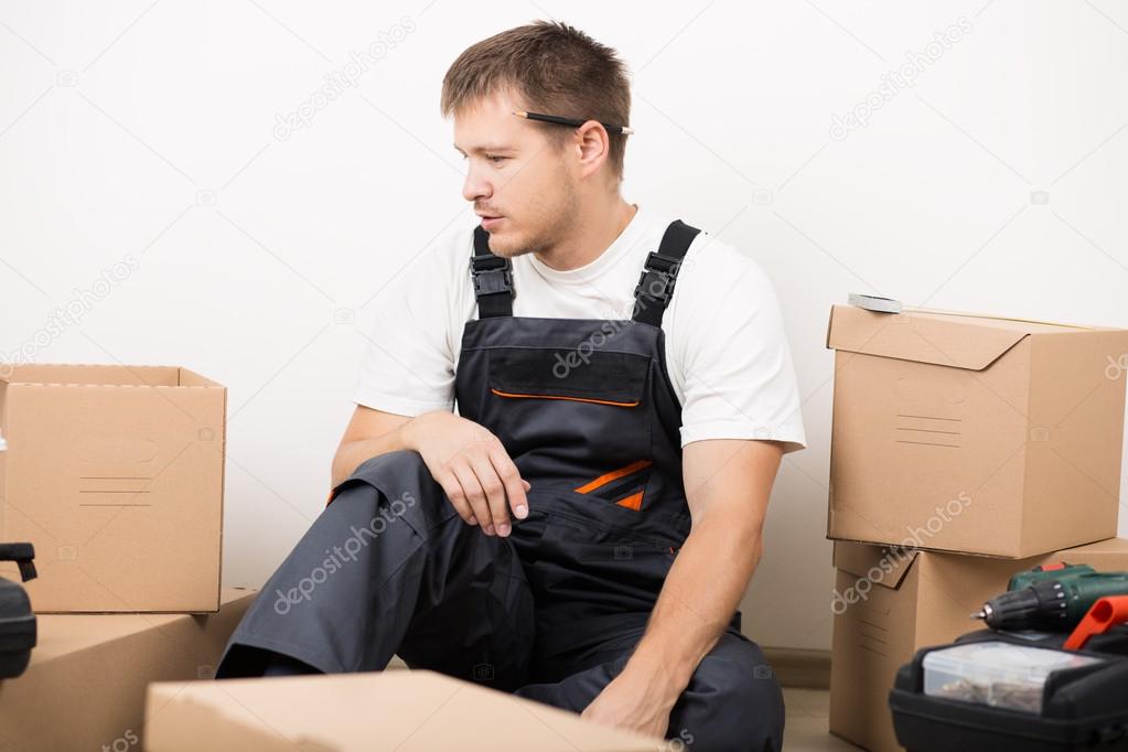 Frustrated man sitting between brown carton boxes