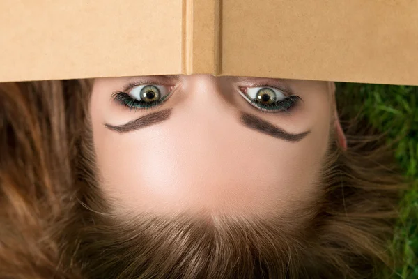 Beautiful young woman hiding her face behind book cover — Stock Photo, Image