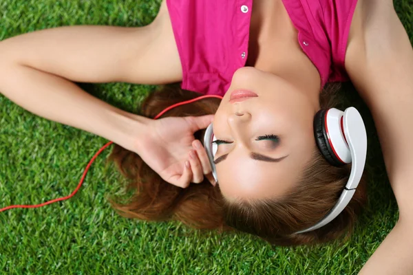 Joven hermosa chica tendida en la hierba en el parque escuchando mu —  Fotos de Stock