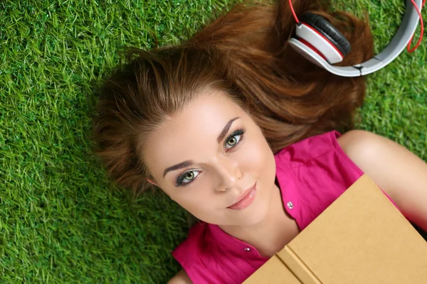 Ung vacker flicka på gräset i parken håller en bok — Stockfoto