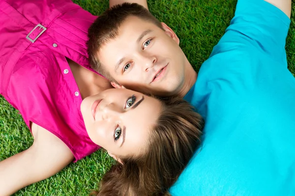 Young beautiful couple laying down together on grass in park — Stock Photo, Image