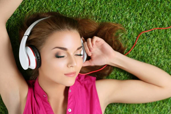 Ung vacker flicka på gräset i parken lyssnar på mu — Stockfoto