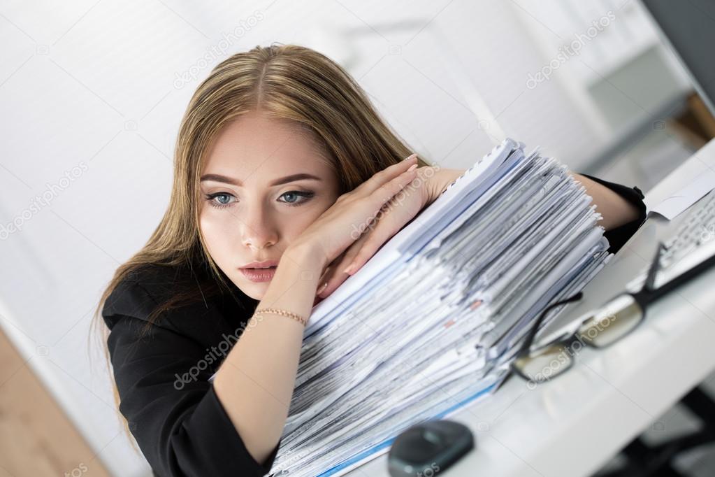 Tired business woman laying on heap of papers at her working pla