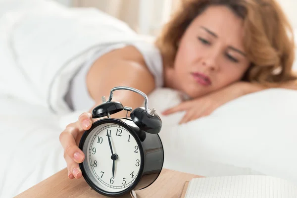 Молодая сонная женщина пытается выключить будильник — стоковое фото