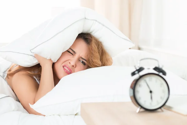 Sleepy girl looking at alarm clock and trying to hide under the — Stock Photo, Image