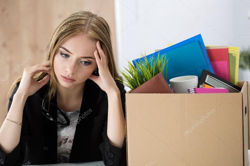 Young dismissed female worker sitting near the carton box with h
