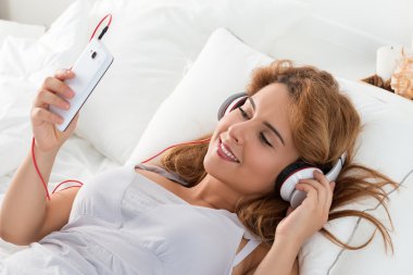 Yatak odasında döşeme ve mus için dinleme genç güzel kadın