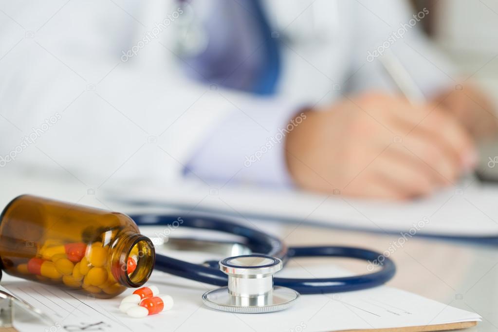 Pills and stethoscope laying on clipping board