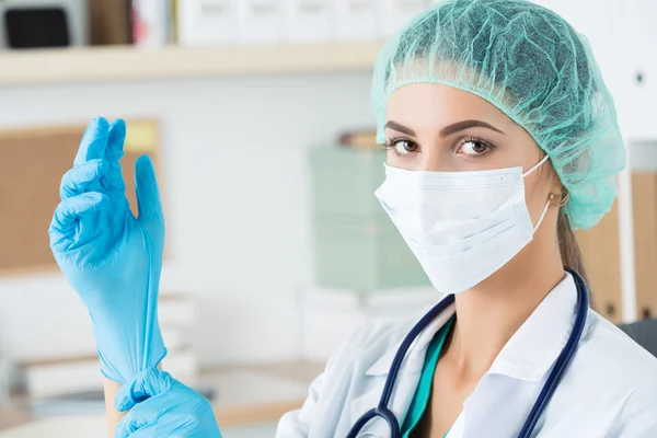 Doctora en máscara protectora y gorra poniéndose azul protegen — Foto de Stock