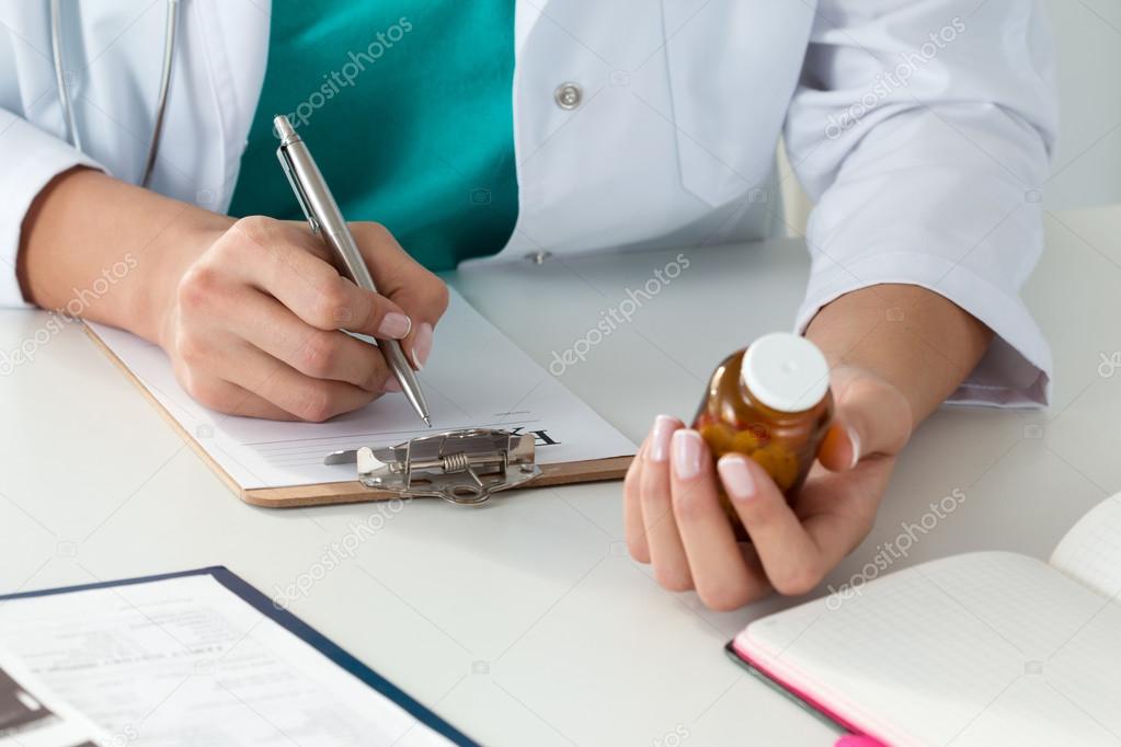 Close-up of doctor's hands writing prescription and holding bott