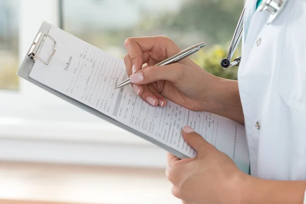 Vista de cerca de las manos del médico femenino llenando el registro del paciente — Foto de Stock