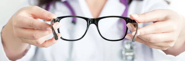 Mãos de médico oculista feminino dando um par de óculos pretos — Fotografia de Stock