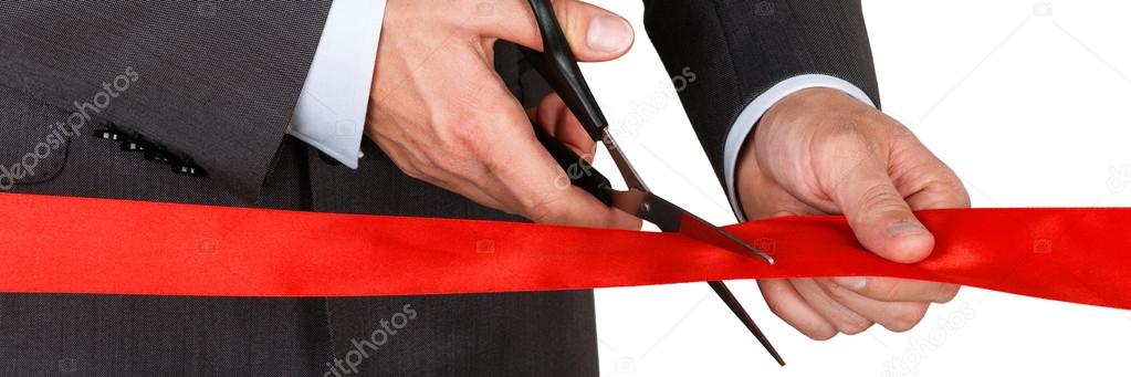 Businessman in suit cutting red ribbon with pair of scissors iso