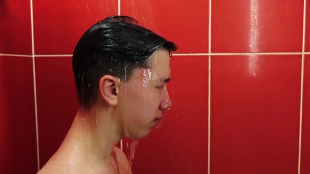 Ein junger Mann unter der Dusche. Ein Teenager wäscht sich im Badezimmer unter einem Strom aus warmem Wasser. — Stockvideo