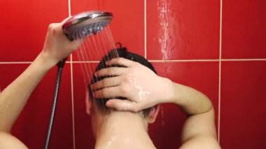 Duşta genç bir adam. Bir genç banyoda sıcak su akıntısının altında yıkanır..