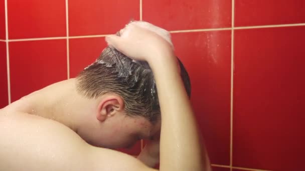 Ein junger Mann unter der Dusche. Ein Teenager wäscht sich im Badezimmer unter einem Strom aus warmem Wasser. — Stockvideo