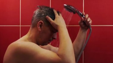 Duşta bir adam var. Orta yaşlı bir adam banyoda sıcak su deresinin altında yıkanır..