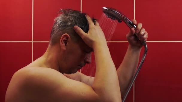 Un hombre en la ducha. Un hombre de mediana edad se lava bajo un chorro de agua tibia en el baño. — Vídeos de Stock