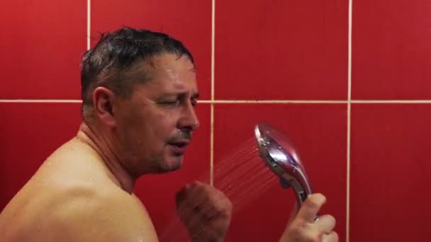 Ein glücklicher Mann singt mit einer Dusche als Mikrofon, während er sich in der Wanne wäscht — Stockvideo