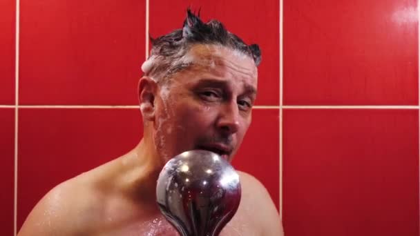 A happy man sings with a shower as a microphone while he washes in the tub — Stock Video