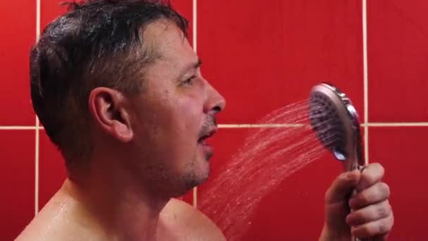 Ein glücklicher Mann singt mit einer Dusche als Mikrofon, während er sich in der Wanne wäscht — Stockvideo