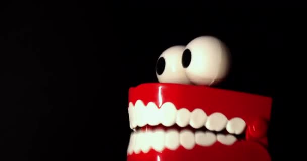 Uma prótese de brinquedo com dentes brancos e olhos grandes, em um fundo preto. — Vídeo de Stock