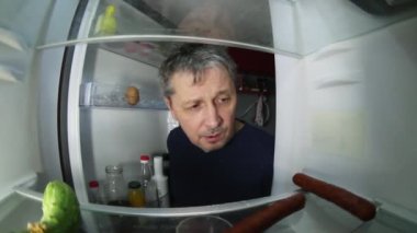 Akşamdan kalma traşsız bir adam buzdolabında içecek ve yiyecek bir şeyler arıyor..