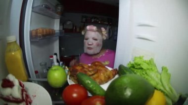 Kozmetik maske takan bir kadın yemek için buzdolabına bakar..