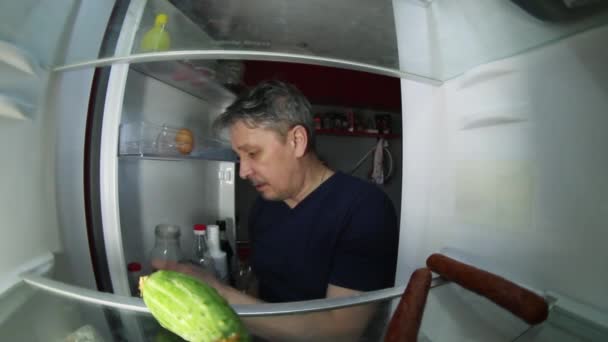 Un hombre sin afeitar con resaca busca en el refrigerador una bebida y algo de comer.. — Vídeo de stock