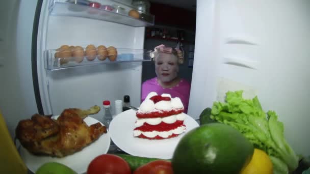 A woman wearing a cosmetic mask looks in the refrigerator for food. — Stock Video