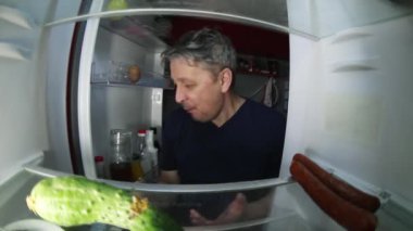 Akşamdan kalma traşsız bir adam buzdolabında içecek ve yiyecek bir şeyler arıyor..