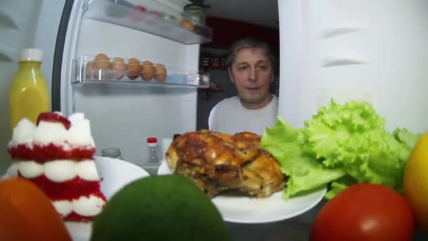 The man looks in the refrigerator for food. To choose from-smoked chicken or fruit with vegetables — Stock Video