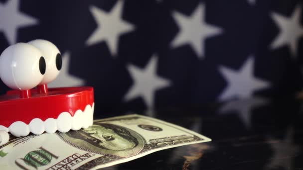 Una protesi giocattolo tiene una banconota da un dollaro tra i denti sullo sfondo della bandiera americana . — Video Stock