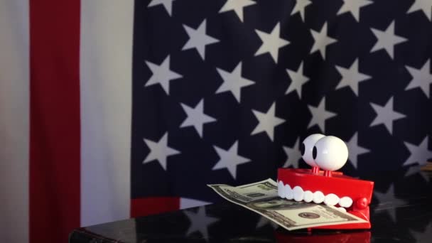 A toy prosthesis holds a dollar bill in its teeth against the background of the American flag . — Stock Video