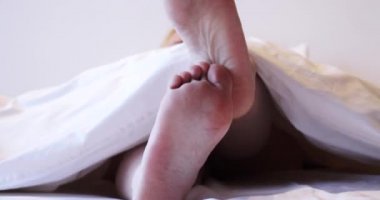 Kadın bacakları battaniyenin altından sarkıyor.