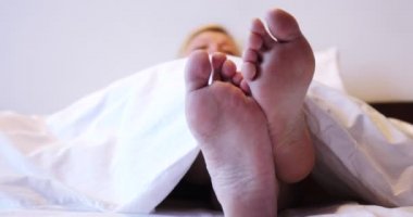 Kadın bacakları battaniyenin altından sarkıyor.