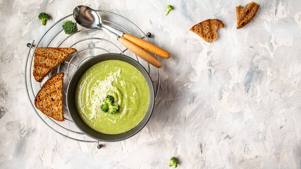 Healthy broccoli green cream soup in bowl over light background. Long banner format, top view. Diet detox food concept.