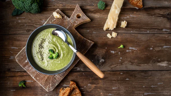 Bowl of broccoli cream soup with parmesan cheese and crunchy croutons on wooden table, top view. — Stock Image Bowl Broccoli Cream Soup Parmesan Cheese Crunchy Croutons Wooden Table Stock Photo