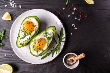 Yumurtalarla pişirilmiş avokado, taze roka, siyah arka planda biber, üst manzara..