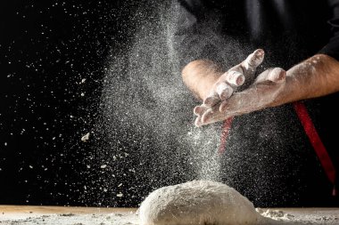 Beyaz takım elbiseli pasta şefi beyaz toz kaplı masaya top hamuru fırlatırken beyaz un havaya uçuyor. Doğa, İtalya, gıda, diyet ve biyoloji kavramı