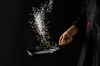 Şefin elinde biberiye, kurutulmuş biberiye ve kırmızı biberli tavada kavrulmuş aromatik tuz pişirmek. afiş, servis menüsü metin için tarif yeri.