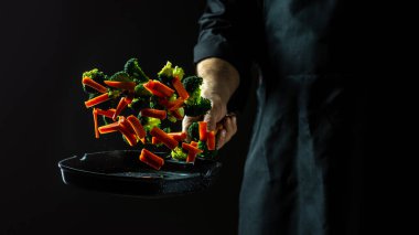 Chef cooking vegetables on a pan. flying vegetables scattering in a freeze motion of a cloud midair on black. clipart