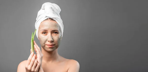 Young beautiful woman in a towel on the head with moisturizing natural mask on face and fresh aloe in hand. Long banner format. space for text,