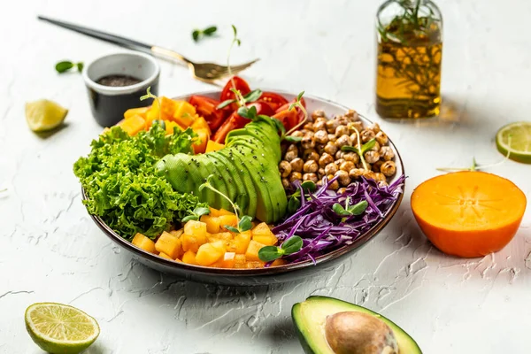 Buddha bowl vegetarian, vegan dish with avocado, tomato, red cabbage, chickpea, fresh lettuce salad, pumpkin, persimmon. Healthy balanced eating. Top view.