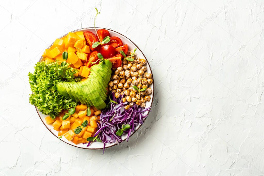 vegan, detox Buddha bowl with avocado, tomato, red cabbage, chickpea, fresh lettuce salad, pumpkin, persimmon. Delicious breakfast or snack on a light background, top view.