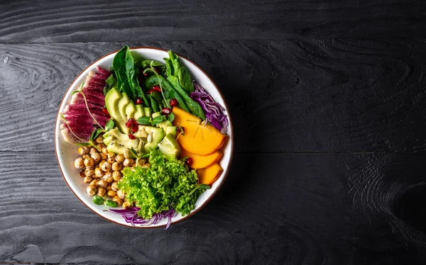 Buddha bowl vegetarian, vegan dish with with roasted chickpeas, avocado, persimmon, spinach, avocado, watermelon radish and seeds. Healthy balanced eating. top view.