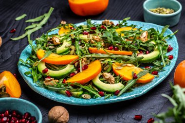 Hurma dilimleri, roka, avokado, kabak çekirdekleri, ceviz, nar, sağlıklı yiyecek üst görüşlü sağlıklı lezzetli salata..