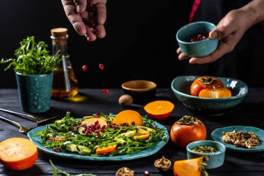 Şefin elinde roka, avokado, kabak tohumu, ceviz ve nar ile vegan hurma salatası pişirmek. Şef 'ten ev yemeği tarifi. Metin için alan alanı olan koyu arkaplan,
