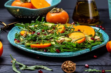 Beyaz ahşap arka planda meyve ve sebzeli taze salata roka, avokado, kabak tohumu, ceviz ve nar ile vegan hurma salatası. Sağlıklı yiyecekler. en üstteki görünüm,