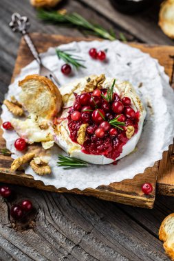 Taze biberiye, kızılcık sosu ve ahşap masada baget ekmeği ile fırında pişmiş camembert peyniri. dikey resim, metin için yer, üst görünüm.